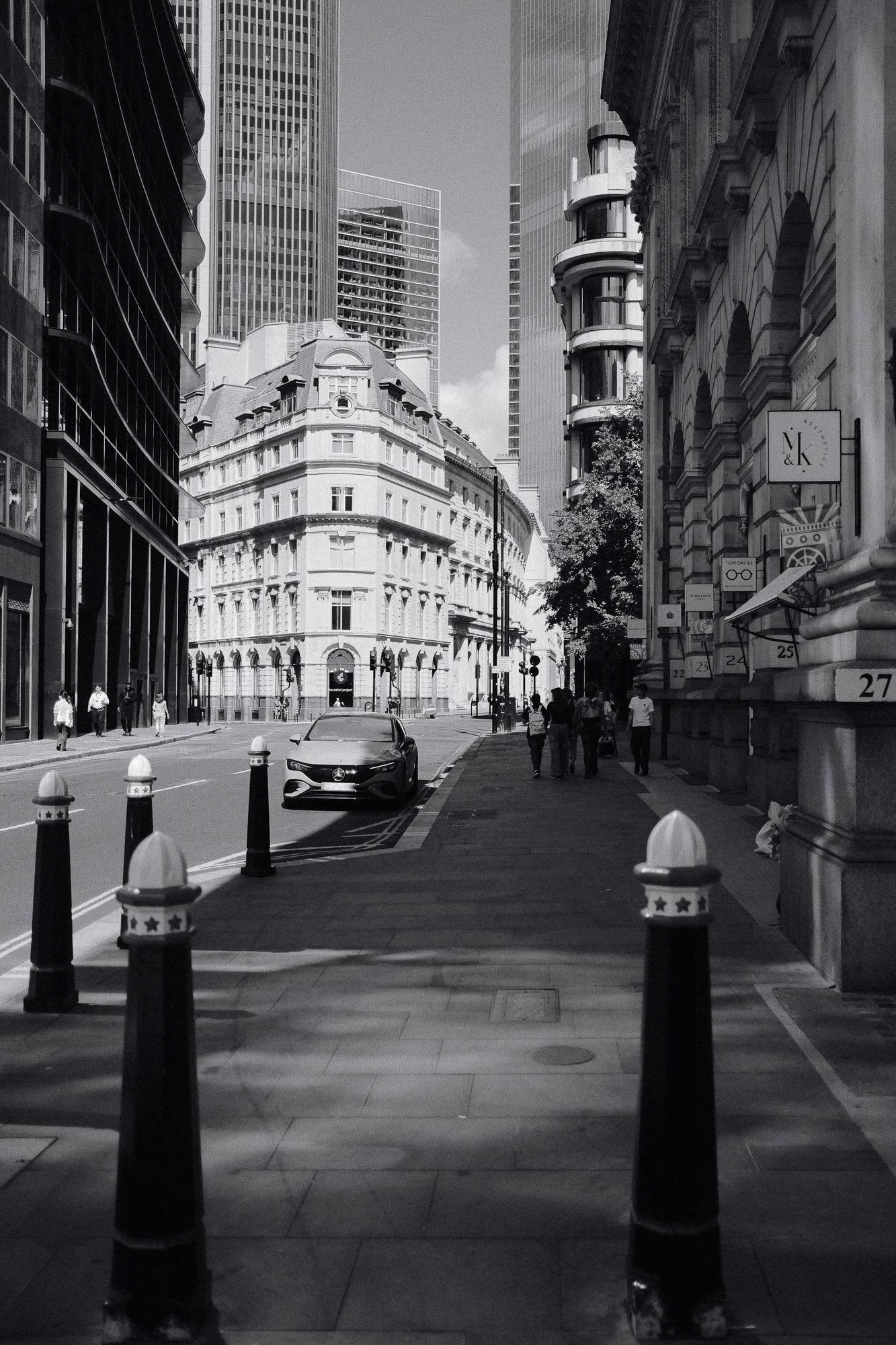 Threadneedle Street in London with a car and people walking on the right side of the road, grayscale